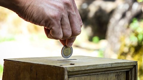 A man's hand putting a coin into a wooden box as donation