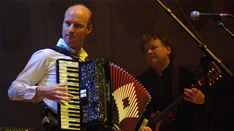 Manus Lunny, Donald Shaw and Capercaillie performing on stage with an accordion featured.