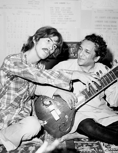 A photograph of George Harrison posing with Ravi Shankar and his sitar. 