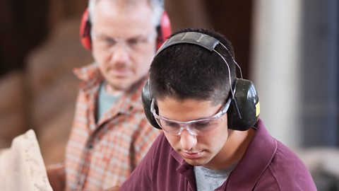 Two workmen shown wearing protective clothing for their eyes and ears.