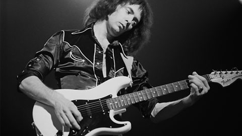 A black and white phorograph of a young Ritchie Blackmore performing on stage. 