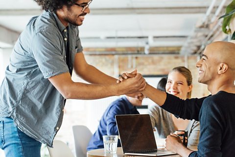 A young man embraces another man's hand, outstretched, networking at a table