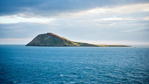 An island with a hill on one side which slopes down to sea level on the other.