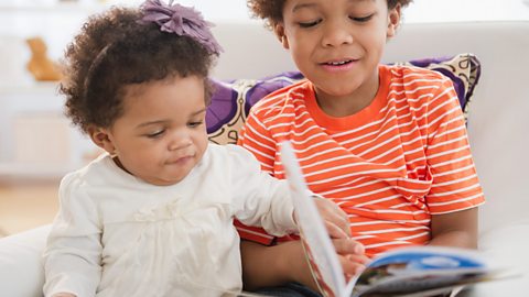 Young boy reading to baby sister.