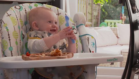 A baby boy smiling in a high chair.