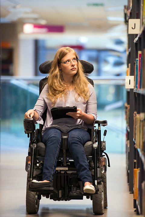 Girl in wheelchair choosing books from library shelves