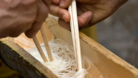 AlexanderLaws/Getty Images Diners must use their chopsticks to catch the slippery noodles as they float by (Credit: AlexanderLaws/Getty Images)