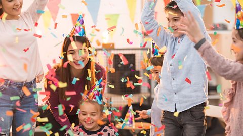 A group of friends and family attend a party, wearing party hats as confetti fills the air.