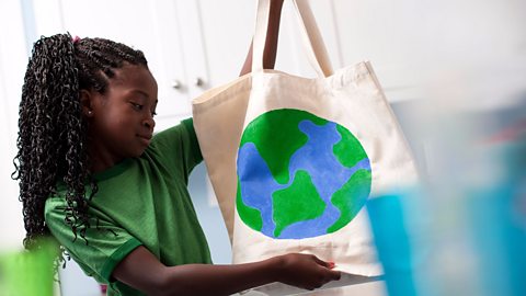 A girl holds up a reusable fabric shopping bag with a drawing of planet Earth on it