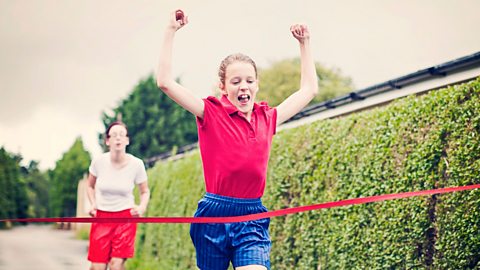 A girl at the finish line of a race raises her hands in the air and celebrates