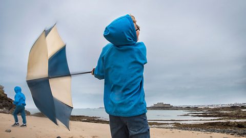 A boy holds on to his umbrella at the beach on a windy day