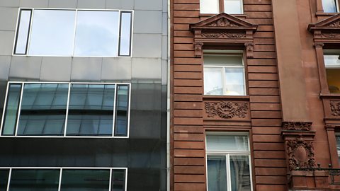 Contrast between old and new buildings - one modern building with large glass windows, and one brown stone building with ornate carvings