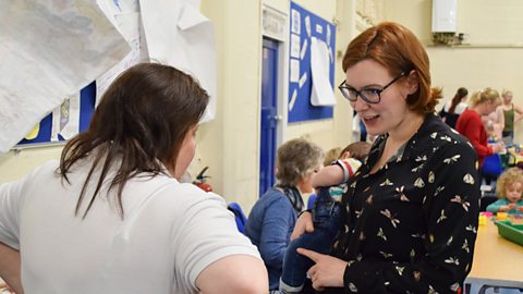 A mum chatting to a playgroup leader while holding her baby.