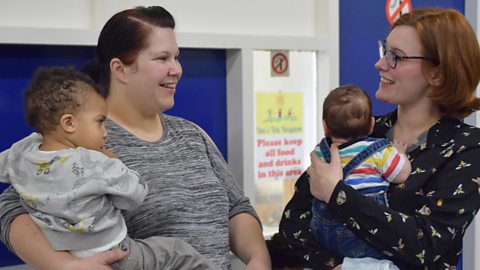 Two mums chatting while holding their babies.