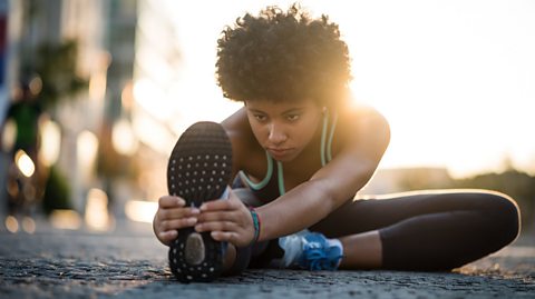 A jogger sitting on the floor doing leg stretches.