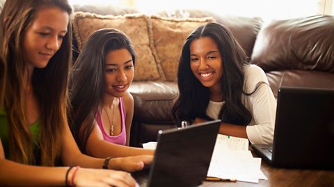 Three students sitting near a brown sofa using laptops to study.