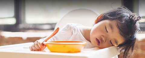 child sleeping in high chair holding spoon after eating