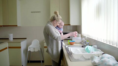 A mum singing to her baby while doing the dishes.