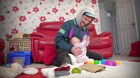 A dad and his baby playing with lots of coloured balls.