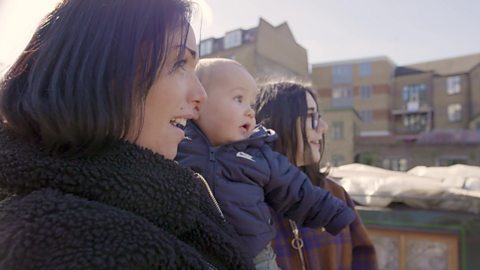 Two women talking to a baby who is looking at something