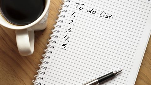 A 'to do list' on a brown desk with number 1 through 5 listed on it and no tasks. There is also a pen and a cup of tea on the desk.