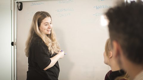 Ellie standing at a whiteboard in a meeting.