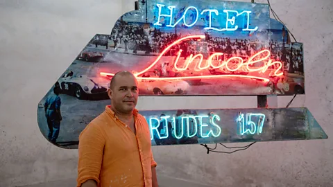 Claire Boobbyer Artist Kadir López in front of one of the many neon signs he's restored on display in the REX (Credit: Claire Boobbyer)