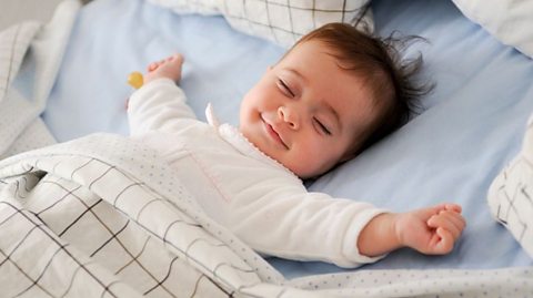 A baby sleeping with a big smile on their face.