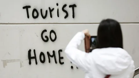 Getty Images A tourist taking a photo of graffiti telling tourists to go home in Barcelona, Spain last year (Credit: Getty Images)