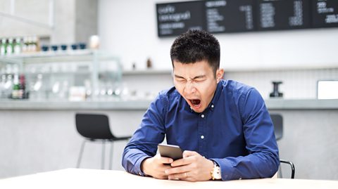 Man yawning looking at his phone