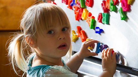 A toddler looks perplexed as she plays with alphabet fridge magnets.