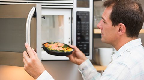 Man putting a plate of food into a microwave oven