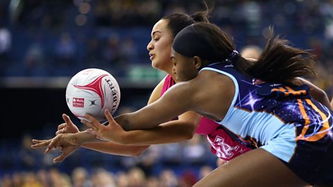 Two netball players running for the ball. 