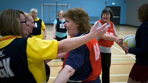 Two older women in netball kit hugging. 