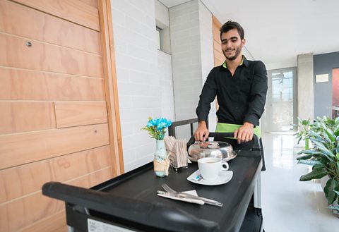 A hotel porter pushing a room service trolley.