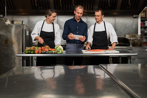 Two chefs having a meeting with their manager in the kitchen.