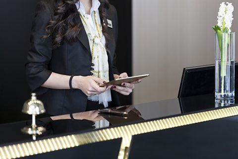 Hotel receptionist using a computerised booking system on a tablet.