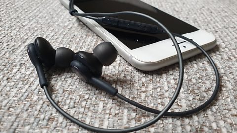 Close up of a mobile phone and earbuds.