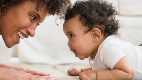 A mum and her baby daughter face to face on the floor.