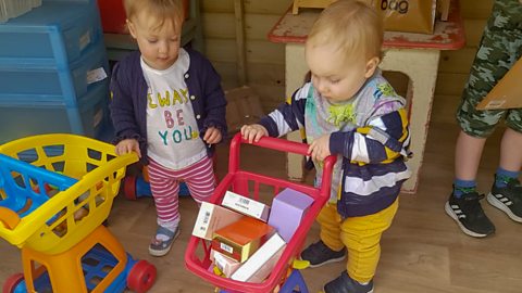 Twins Aria and Isaac playing with toy shopping trolleys.