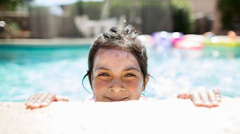 Child peeking out of a pool with sun cream streaks on their face.