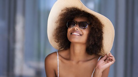 A woman of colour in sunglasses and a sun hat.