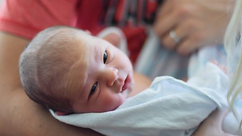 A baby turning away from their mum as they're being held.