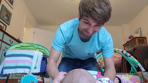 A dad pulling his face as he changes his baby's nappy.