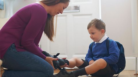 A mum putting her child's shoe on.