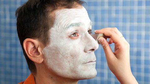 A person having white makeup applied to their face with a sponge.