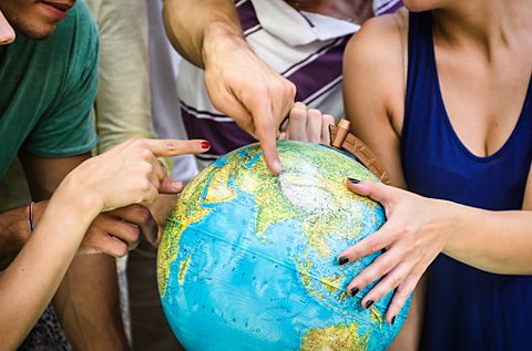 Students pointing at different countries on a globe.