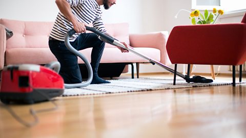 A man using a vacuum cleaner on the floor.