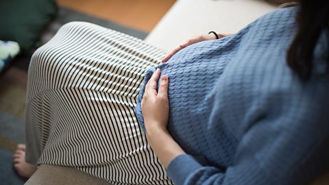 Pregnant woman sat down holding her bump