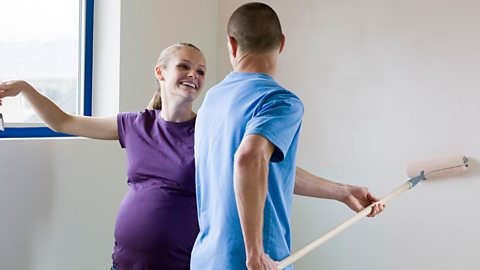 A pregnant woman and a man decorating a room